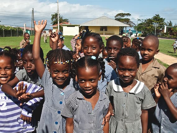 A large group of children in patterned uniforms gathered together outdoors at Negril Basic School