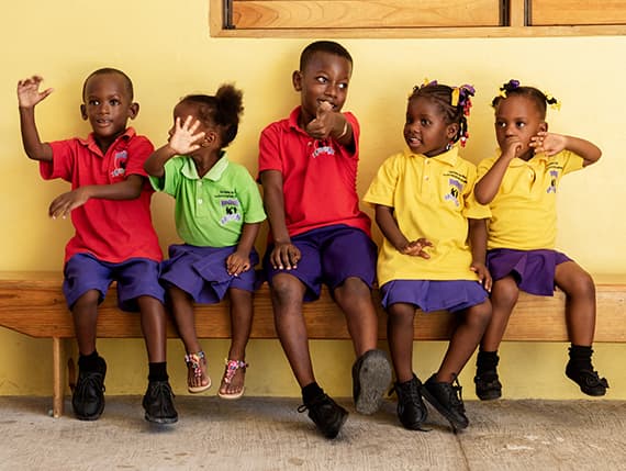 Children in school uniform sitting together against a yellow wall at the Sav Inclusive School